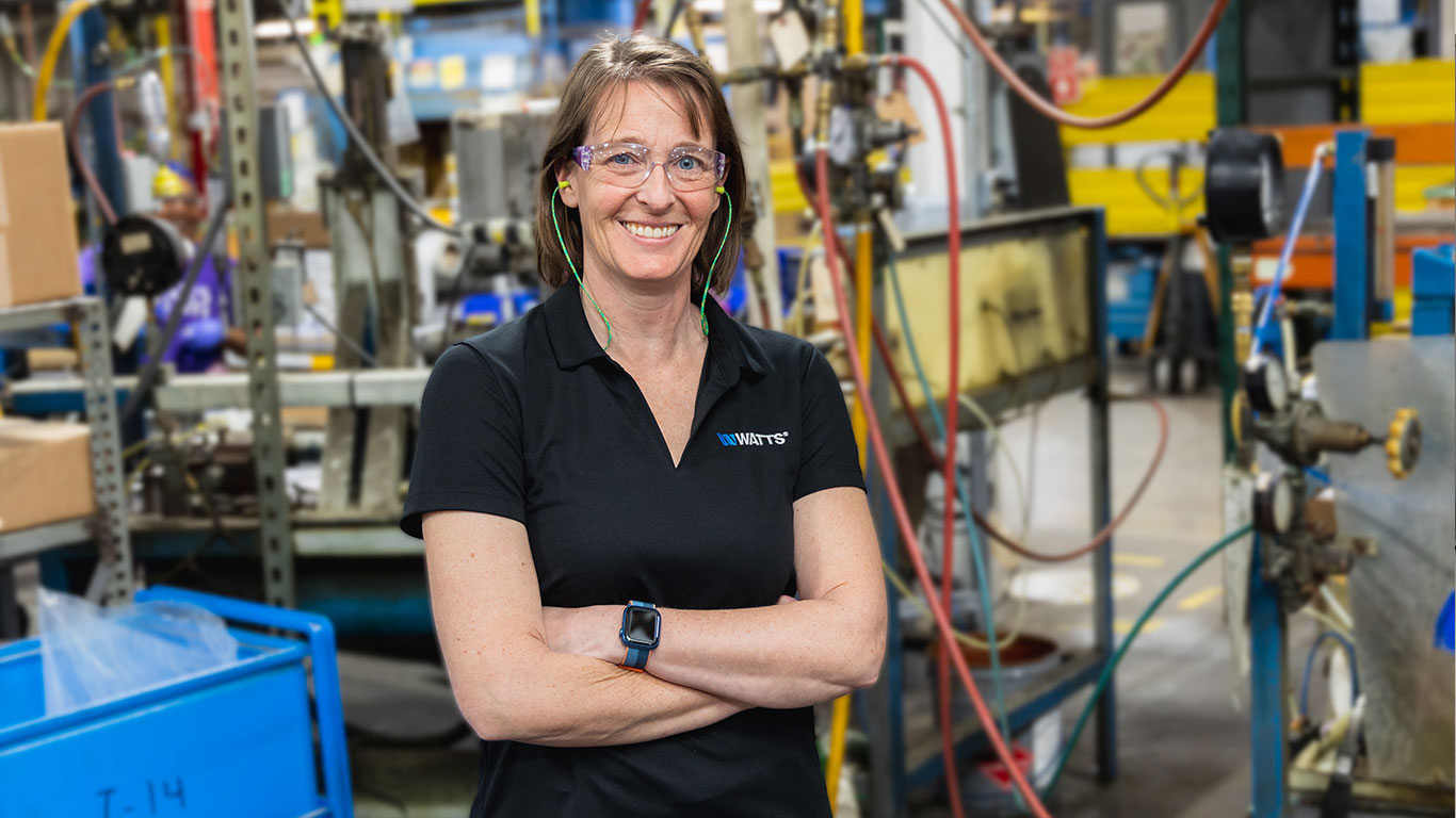 Female factory employee posing in front of machinery.