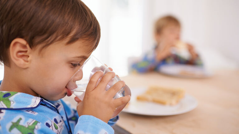 Child drinking water from a glass at a table 